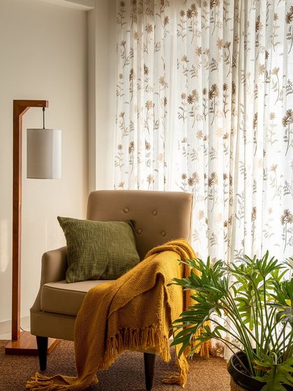 Every home needs cozy corners. Here, a comfortable armchair, a warm throw, and soft, filtered light from the floral curtains create the perfect spot to read and relax.