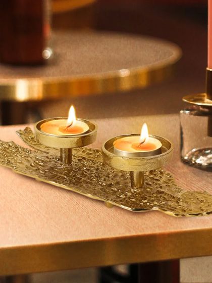 A warm, atmospheric shot of a textured golden tea light holder on a dinner table. The lit candles create a cozy ambiance, perfect for showcasing decorative items.