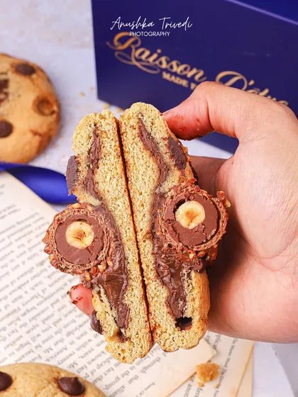 A close-up of a hand holding a cookie that's been split open to reveal a Ferrero Rocher inside. This "reveal" shot is super effective for showcasing indulgent fillings.