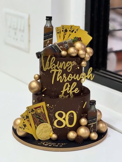 Turning 80 and still vibing through life. This classy two-tier chocolate cake celebrates a timeless spirit with a dash of whisky, golden playing cards, and good vibes only.