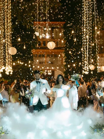 Walking into forever through a magical cascade of lights and ethereal smoke. This is the grand entrance, a moment filled with wonder and the shared excitement of starting a new life together, surrounded by everyone they love.
