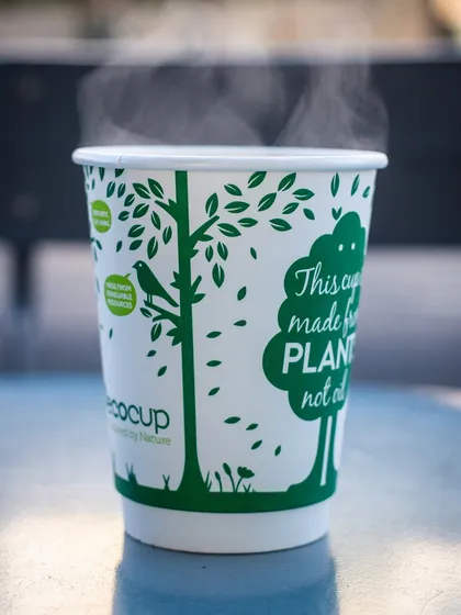 A steaming hot cup of coffee in a branded eco-cup. The visible steam instantly communicates warmth and comfort, perfect for a winter's day.
