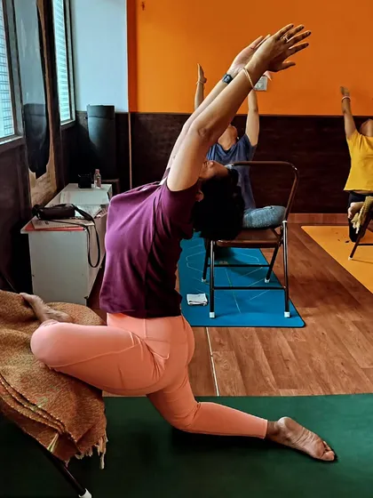 Yoga is for everyone, and I use props like chairs to make it accessible. Here, a student uses a chair for support in a modified Anjaneyasana (low lunge), allowing for a deep, safe stretch in the hips and spine, regardless of flexibility or mobility levels.