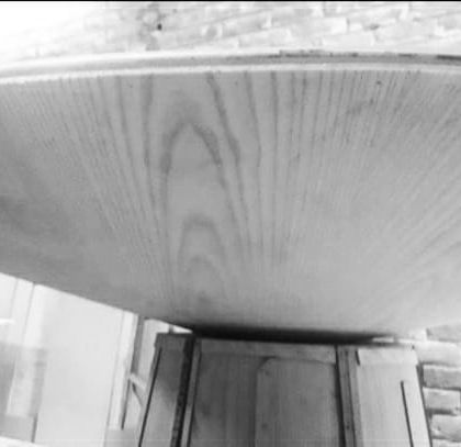 The process of applying ash wood veneer to the table. This close-up shows the beautiful grain of the wood as it's carefully fitted to the curved surface of the tabletop.