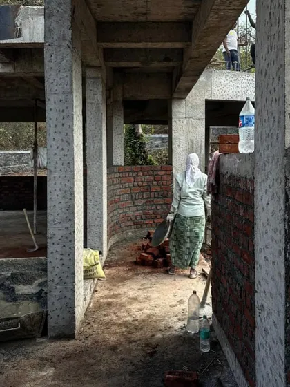 A worker stands inside a curved brick wall under construction. This image shows the process of laying out complex forms on site, translating architectural drawings into physical reality.