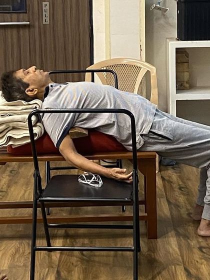 A student resting in a supported backbend over a chair and bench. This setup is excellent for releasing fatigue and calming the mind after a long day.