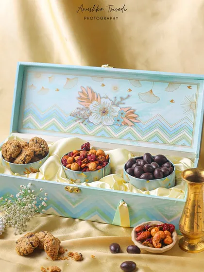 A pastel blue hamper box filled with cookies and chocolate-coated nuts. The soft satin lining and delicate flowers give it a very premium and elegant feel.