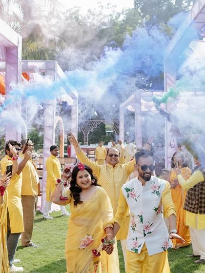 The couple's grand entrance at their Haldi, celebrated with bursts of colorful smoke. This moment is all about energy and joy. *Note: This image seems miscategorized as Mehendi but fits the fun, carnival vibe.*