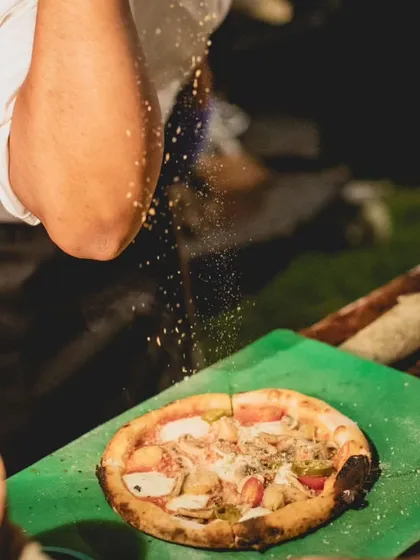 The final seasoning is artfully sprinkled over a freshly made pizza. This action shot captures the craftsmanship and attention to detail that defines our live cooking experiences.