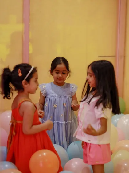Three friends in a sea of pastel balloons, sharing secrets and smiles during a unicorn party.