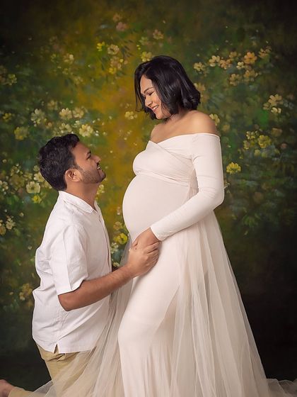 A classic pose of devotion, with the father-to-be kneeling to connect with his child. The floral backdrop adds a touch of romance and nature.
