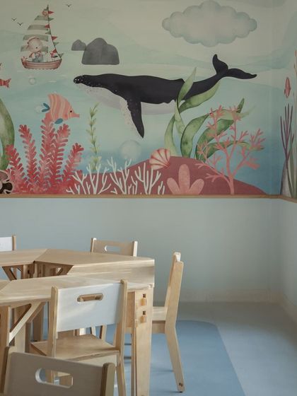 A close-up of the modular birch ply tables and chairs in the aqua classroom, with the vibrant underwater mural in the background. The furniture is lightweight, durable, and free of plastics.