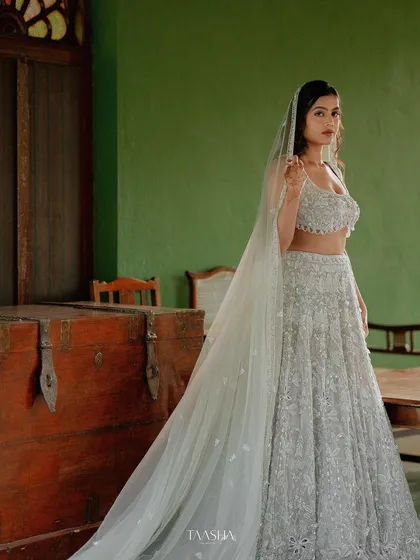 A bride in a modern, ethereal white lehenga with a long veil, standing in one of our heritage suites. The contrast is simply stunning.
