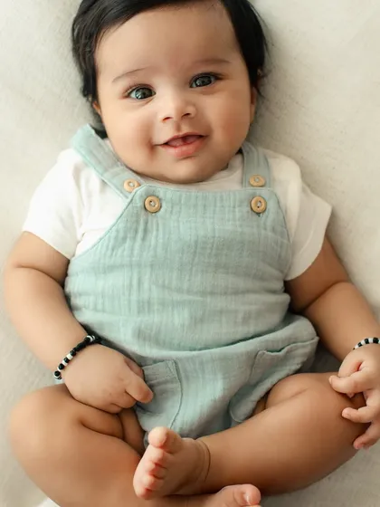 A sweet and simple portrait of a happy baby. Dressed in a cute muslin romper, this little one's bright eyes and gentle smile are the focus of the shot.