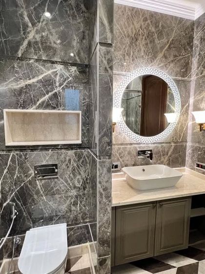 This bathroom at C-257 showcases a beautiful vanity with an undermount sink, a large decorative mirror, and walls clad in stunning grey Italian marble.