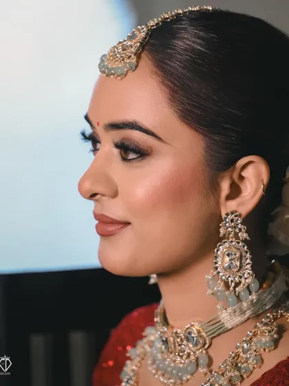 A profile shot that highlights the bride's flawless makeup and the stunning details of her earrings and maang tikka. This is a modern, elegant bridal portrait.