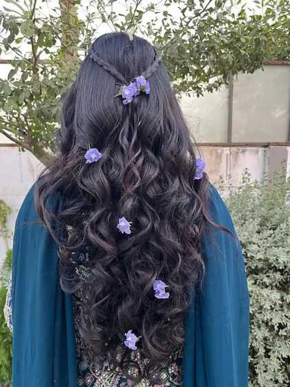 A whimsical and romantic hairstyle with loose waves and small purple flowers scattered throughout. Perfect for a mehendi or outdoor event.