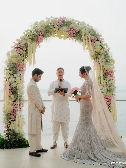 A beautiful pastel floral arch frames the couple during their vows at a seaside wedding in Goa, with the ocean as a natural backdrop.