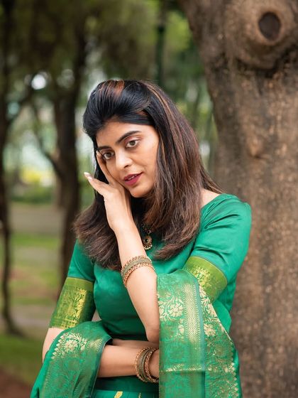 An expressive and thoughtful pose in a traditional green saree. This outdoor portrait captures a moment of quiet elegance.