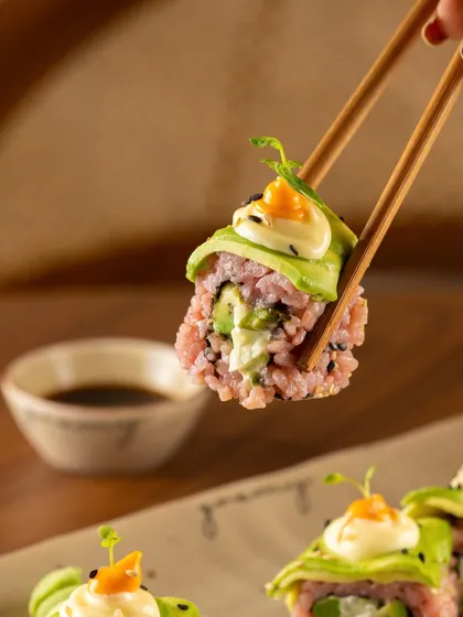 An avocado-wrapped sushi roll held up to the camera. This shot highlights the fresh ingredients and intricate construction.