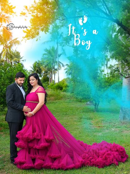 A gender reveal photo using blue smoke to announce "It's a boy!". The couple is dressed in elegant attire, with the mother-to-be in a beautiful ruffled gown.