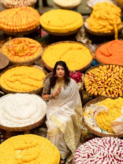 A powerful and centered portrait amidst the flowers. Her pose is confident, and the composition is rich with color and culture.
