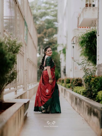 The bride looking back with a smile, showcasing the beautiful drape of her traditional half saree in red and green.