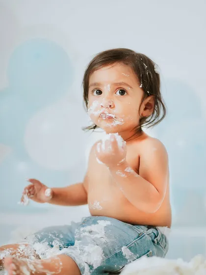 A classic cake smash photo, with frosting on his face and a handful of cake ready to go. The simple blue and white theme keeps the focus on him.