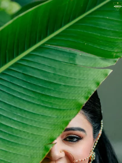 An artistic and creative close-up, with the bride's eye peeking from behind a large green leaf. A unique and captivating bridal shot.