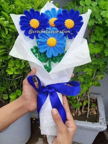 Holding a beautiful bouquet of blue daisies in two different shades, tied with a matching blue ribbon. This forever bouquet is a wonderful, lasting gift.