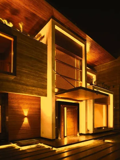 This is the entrance to the 'Kohinoor' residence, a project where light was used to enhance the natural warmth of the stone and wood. The design employs a combination of recessed linear lighting, subtle uplights, and focused downlights to create an inviting and luxurious welcome.
