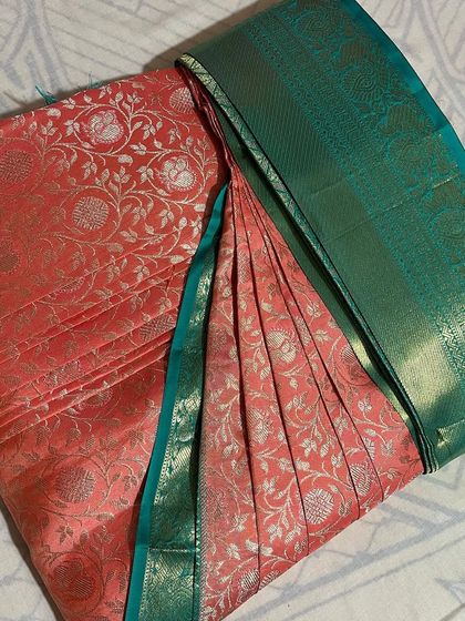 This peach-colored saree with a green border has a delicate floral pattern. Careful pleating ensures the design is not disturbed.