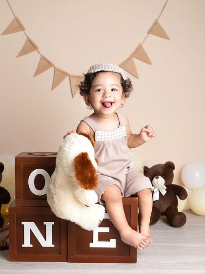 This little boy is all smiles for his first birthday. The rustic, neutral theme with teddy bears and wooden blocks creates a warm and timeless feel for a milestone photoshoot.
