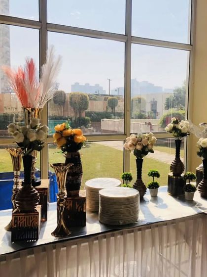 The appetizer and plate station for a private party, set against a large window with a garden view. The elegant vases and floral arrangements enhance the sophisticated ambiance.