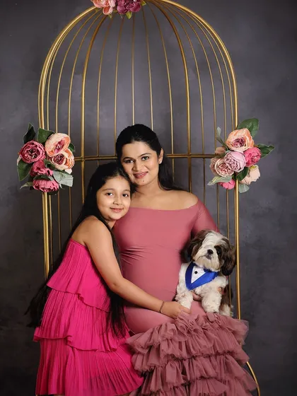 A mother-to-be with her daughter and their beloved pet. This shot, set in a beautiful golden birdcage prop, highlights the love that fills their growing family.