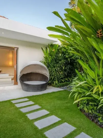A private outdoor seating area connected to a bedroom, featuring a perfect lawn and a simple stone path. The surrounding tall, leafy plants provide privacy and a sense of enclosure.