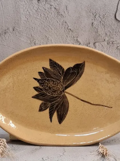 This organic, oval-shaped plate features a single, beautifully detailed lotus flower. It's a versatile piece that can be used for serving scones, sushi, or simply as a decorative item in your home.