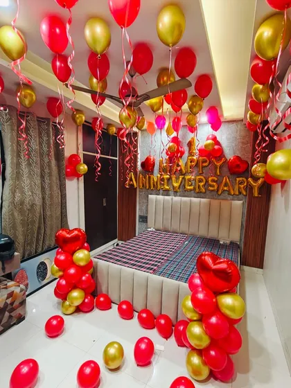 A classic anniversary room decoration in red and gold. The room is filled with balloons floating to the ceiling, balloon bouquets, and a large "HAPPY ANNIVERSARY" foil banner above the bed to surprise your loved one.