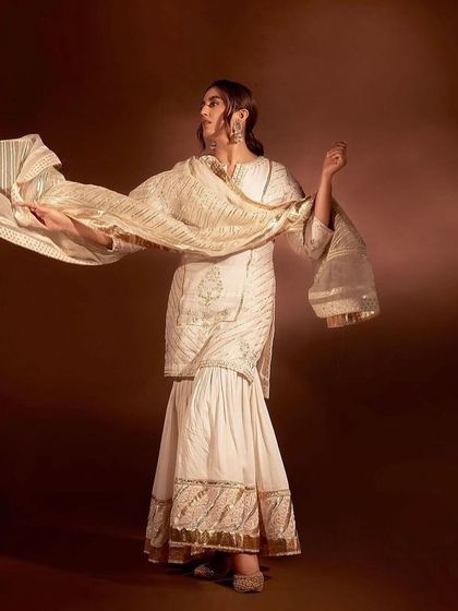 An ivory sharara set with gold gota patti work, a traditional and festive look perfect for a wedding.