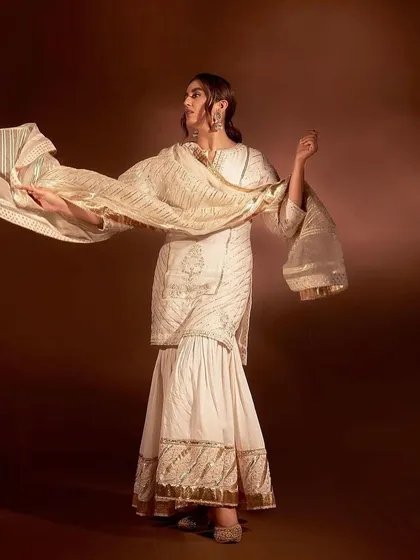 An ivory sharara set with gold gota patti work, a traditional and festive look perfect for a wedding.