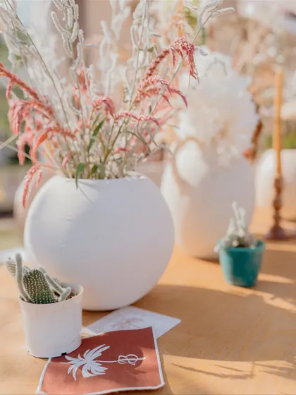A close-up of the delicate table decor, featuring white vases with pink-tinged dried flowers and small cacti, adding a subtle touch of color to the neutral theme.