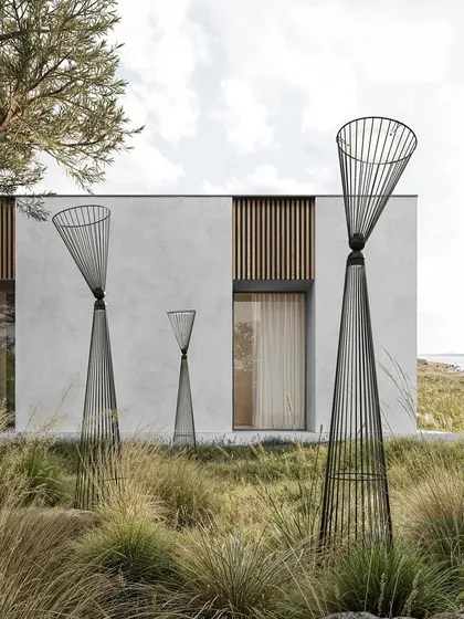 A group of Ikonika floor lamps of different sizes is arranged in an outdoor landscape, appearing like sculptural totems in the wild grass.