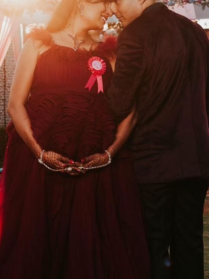 A romantic, sun-kissed photo of an expecting couple. The deep red of the gown looks stunning against the warm light of the setting sun.