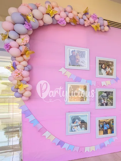 A beautiful memory wall from a butterfly-themed first birthday. We created a soft pink backdrop and arranged framed photos, accented with a pastel balloon garland, to tell the story of the little one's first year.