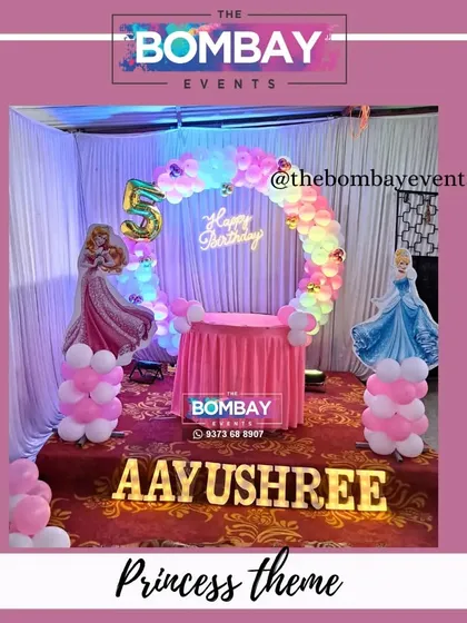 A lovely princess theme for a 5th birthday. This setup features a circular balloon arch, a pink cake table, and cutouts of Cinderella and Sleeping Beauty.