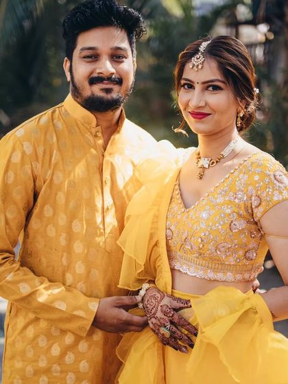 A perfect Haldi look. The groom is wearing a simple kurta made from pure silk mustard-colored fabric with a subtle booti pattern, coordinating with the bride's yellow lehenga.