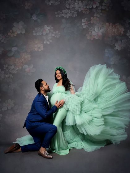 A romantic couple's portrait where the dad-to-be kneels to embrace the baby bump. The mom-to-be's mint green ruffled gown fills the frame, creating a soft and dreamy atmosphere.
