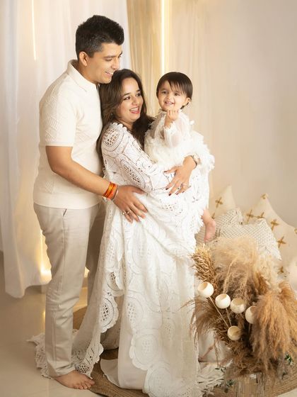 A full-length portrait of a family sharing a happy moment. The warm lighting and light-colored wardrobe contribute to the bright and airy feel of the photo.