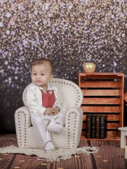 Dressed in a smart white and red suit, this baby sits like a little gentleman against a sparkling glitter backdrop, creating a glamorous and celebratory portrait.
