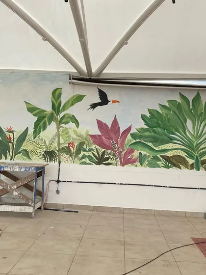 We call this our tropical paradise. We transformed the walls of a restaurant with a misty forest theme, covering even the doors to create a seamless, immersive jungle experience with colorful birds and lush greenery.